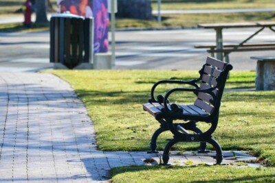 Foto einer Bank entlang eines Weges mit einem Mistkübel im Hintergrund