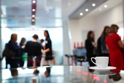 Foto mit scharf gestellter Kaffetasse im Vordergrund, sprechende Menschen im Hintergrund verschwommen