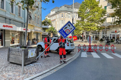 Bauarbeiter tragen ein Begegnungszone-Schild zu einer temporär abgesperrten Straße