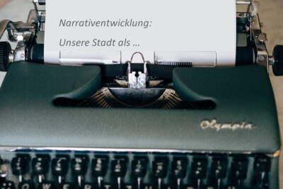 Schreibmaschine, die den Text: "Narrativentwicklung: Unsere Stadt als..." geschrieben hat.
