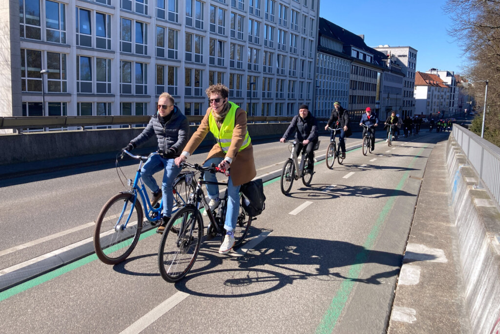Radgruppe fährt sanft eine Brücke auf einem 2 Richtungsradweg hinauf. Strahlender Sonnenschein. Tiefer Sonnenstand