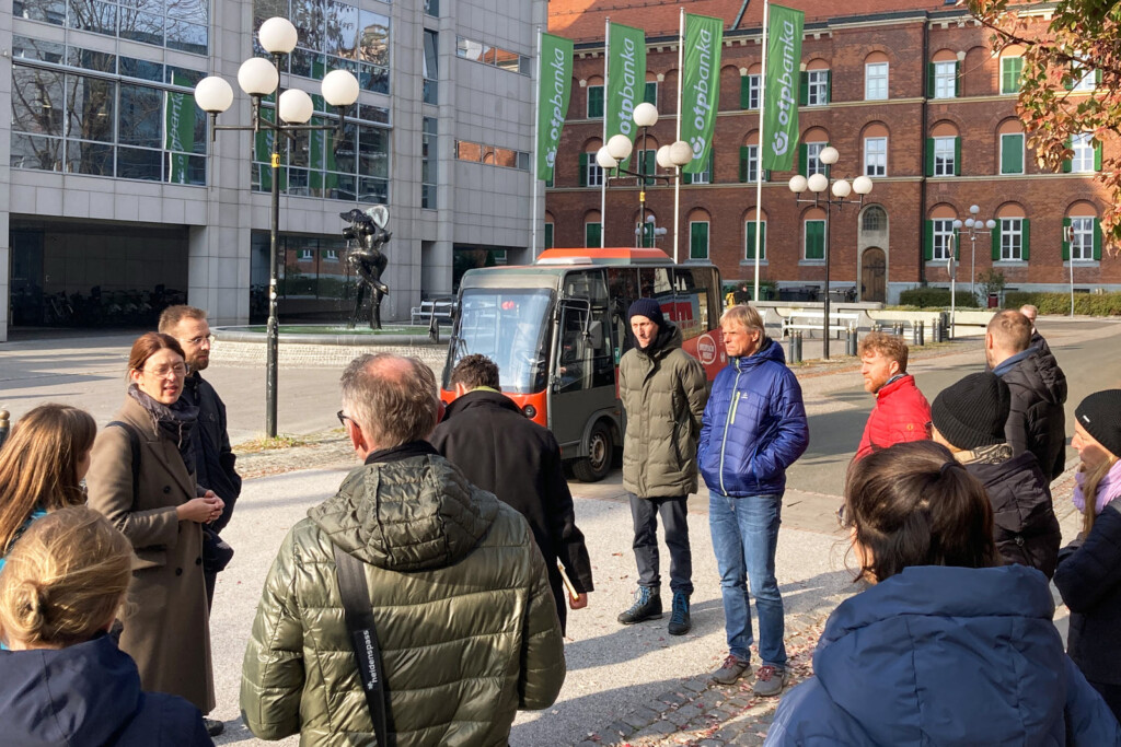 Straßenszene. Im Hintergrund ein e-Minibus. Im Vordergrund eine Personengruppe bei einer Führung.
