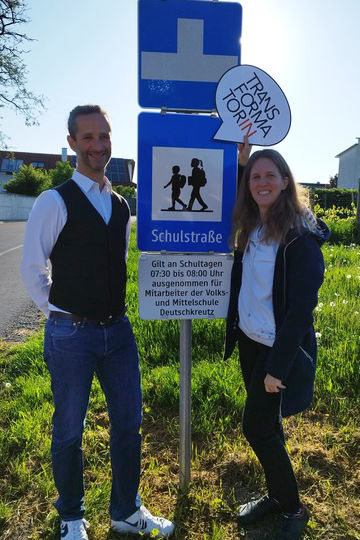 2 Personen links und rechts. In der Mitte ein Verkehrsschild Schulstraße. Darüber ein Schild Sackgasse