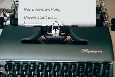 Schreibmaschine, die den Text: "Narrativentwicklung: Unsere Stadt als..." geschrieben hat.