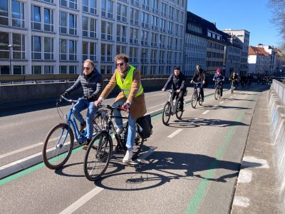 Radgruppe fährt sanft eine Brücke auf einem 2 Richtungsradweg hinauf. Strahlender Sonnenschein. Tiefer Sonnenstand