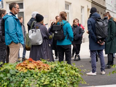 Transformatorinnen Workshop Gruppe steht auf der Straße und lauscht gespannt der/dem Vortragenden.