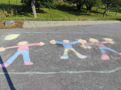 Kinderkreidezeichnung von 3 Personen auf einer Straße. Angrenzend an die Straße eine Streuobstwiese.