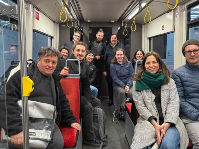 Viele Menschen schauen in einer Straßenbahn in die Kamera. Die meisten sitzen.