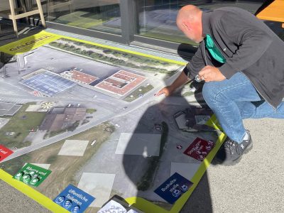 Großer Bodenplan des Ortsteils Galgenul, verschiedene Gestaltungselemente am Rand. Ein Mann platziert eine Gestaltungsidee am Bodenplan