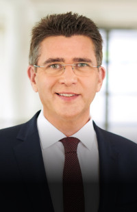 Mann, grüne Augen, fassungslose Brille, dunkelblaues Sakko, rote Krawatte