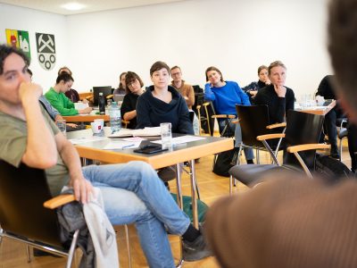 Workshop Diskussions-Situation. Mitglieder des Projektteams sitzen an unterschiedlichen Tischen in gemeinamer Diskussion