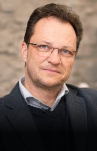 Portraitbild von Jens de Buck. Sakko, Pullover, offenes Hemd