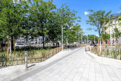 Christian-Broda-Platz mit Begrünung, Sitzgelegenheiten und taktilem Leitstreifen.